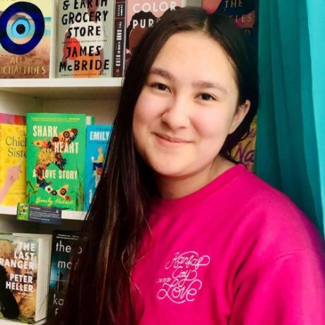 Halley Vincent, fourteen-year-old owner of Seven Stories, stands in front of a bookshelf.
