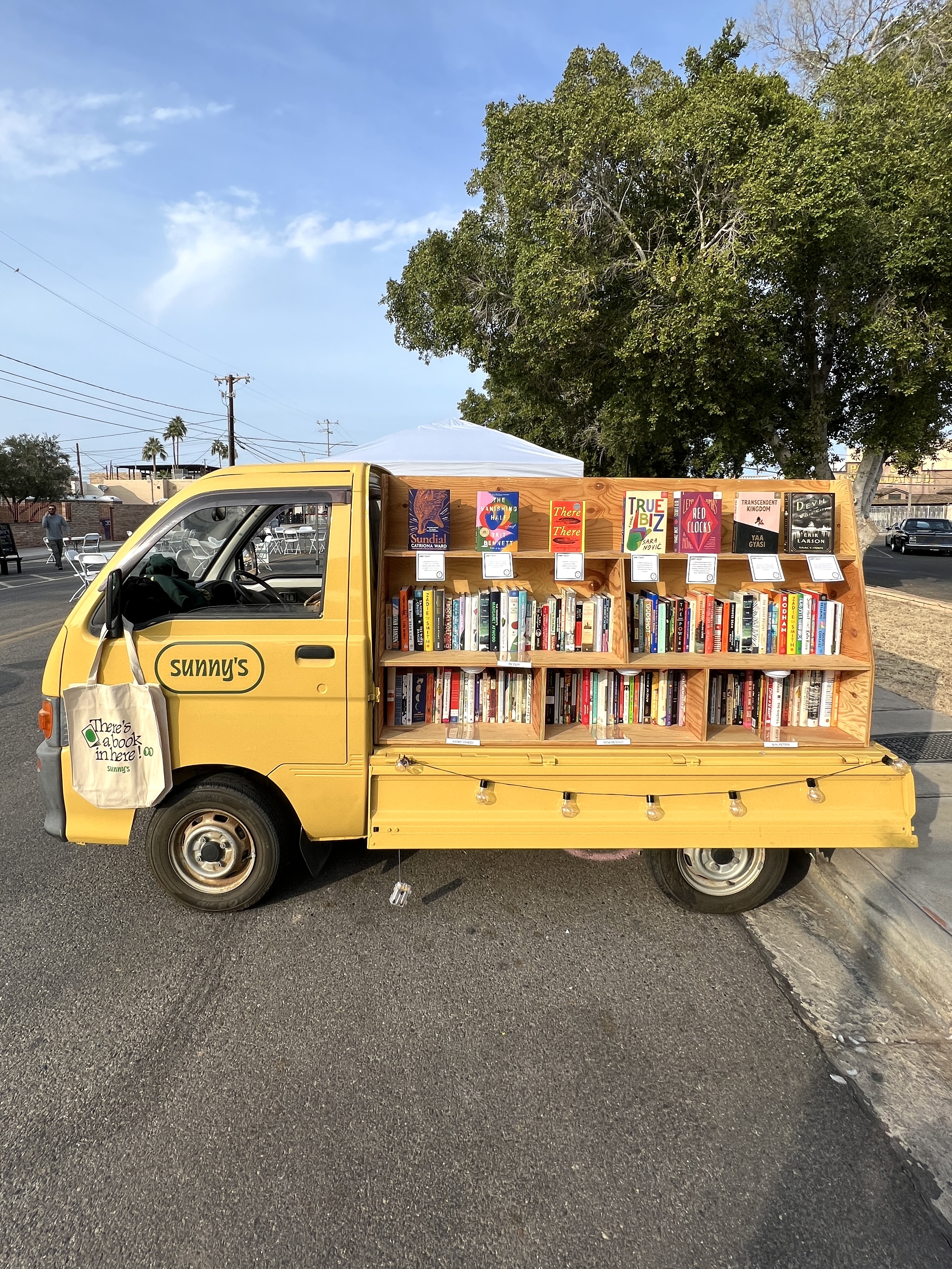 A yellow mini truck with a shelf of books.